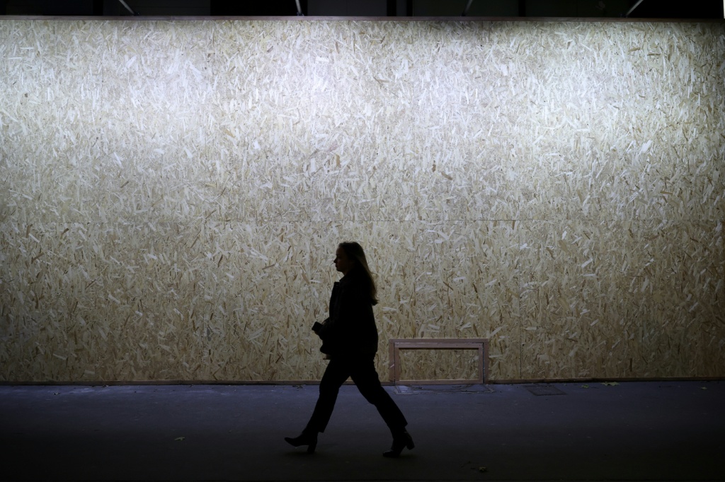 A woman walks past a shop window of the jeweler and watchmaker Cartier, entirely hidden with wooden panels ahead of a demonstration planned for Saturday — SIMON WOHLFAHRT / AFP