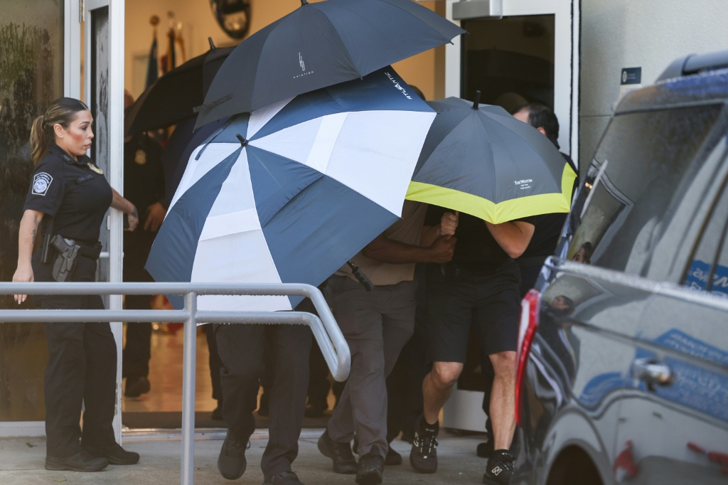 US agents with umbrellas shield people leaving Opa-Locka Executive Airport in Florida shortly after Brazil's Flavio Bolsonaro and his family arrived on a private jet — Ricardo Arduengo / AFP