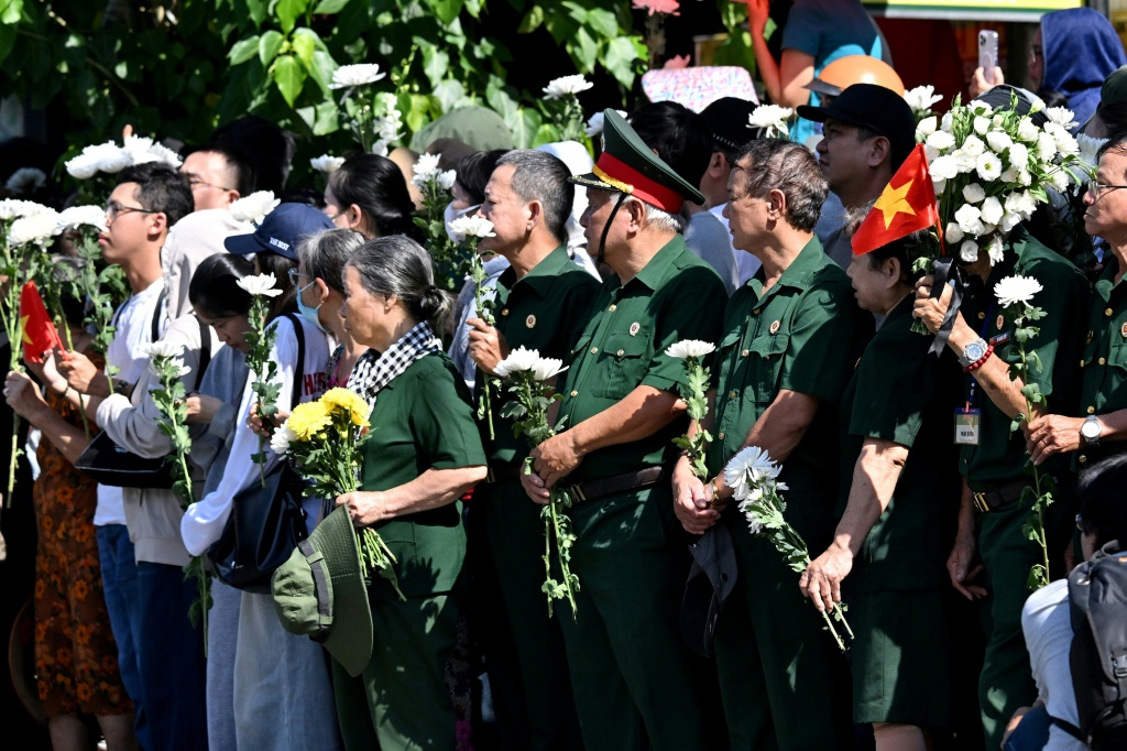 People gather with flowers by a roadside as they wait for the vehicles transporting the remains of fallen soldiers to pass by in Ho Chi Minh City — Nhac NGUYEN / AFP