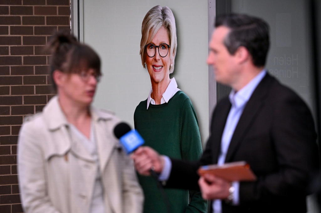 A TV crew works in front of a portrait of Australian politician Helen Haines (C) outside her office in the northern regional city of Wangaratta, about 250 kilometres north-east of Melbourne on October 20, 2026.  Australian independent lawmaker Helen Haines underwent surgery overnight but remains in a critical condition after being struck deliberately by a car in an attack, Prime Minister Anthony Albanese said on October 20. Political violence is rare in Australia, but law enforcement have documented a stead