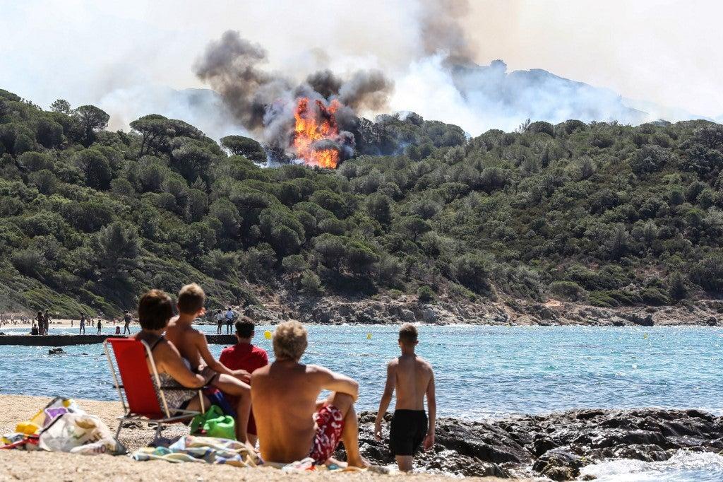 People enjoy the beach as they look at a forest fire in La Croix-Valmer, near Saint-Tropez, on July 25, 2017. Valery HACHE / AFP