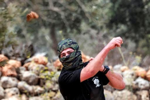 A masked man hurls stones at Palestinians who had gathered for the annual olive harvest season, during an attack by Israeli settlers on the Palestinian village of Beita, south of Nablus in the occupied West Bank, on October 10, 2025. — Jaafar ASHTIYEH / AFP