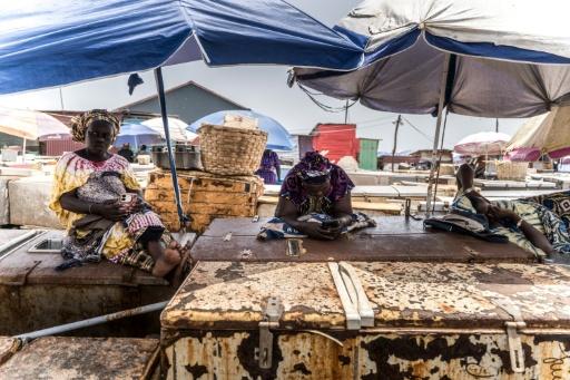 Des poissonniers se reposent sur leurs réfrigérateurs au point de débarquement des poissons à Tanji, en Gambie, le 12 septembre 2026, alors que les coupures d'électricité prolongées rendent difficile la conservation de leurs prises — MUHAMADOU BITTAYE / AFP